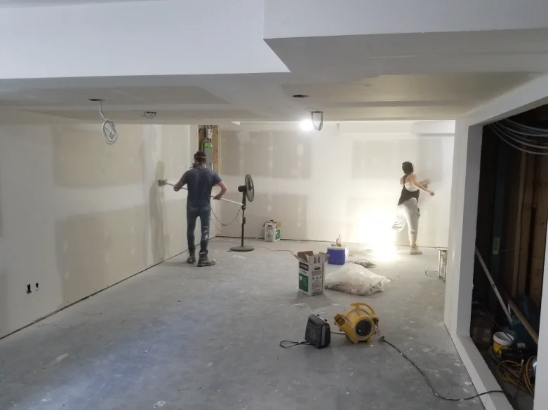Two drywall finishers taping and mudding seams in a room under construction