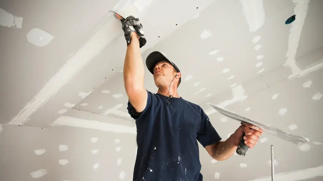 Drywall finisher smoothing joint compound over a replaced section of ceiling